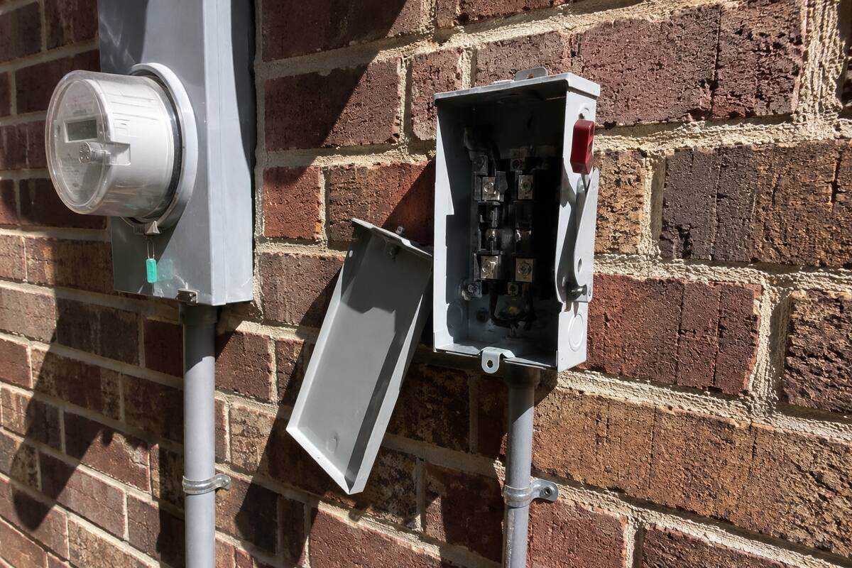Outdoor air conditioning disconnect box mounted on a brick wall with the cover off, conduit running down to the ground