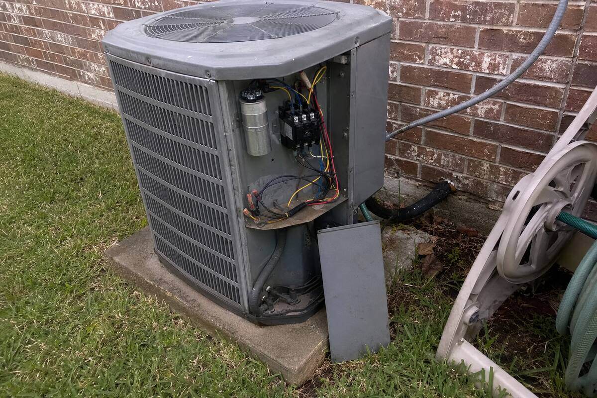 Electrical access panel removed from an outdoor condenser unit, contactor and capacitor visible inside