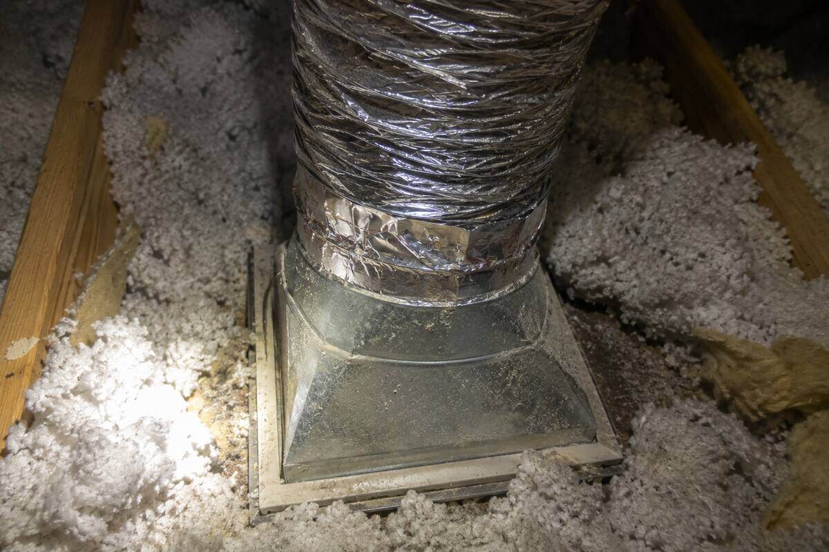 Flexible duct joining a sheet metal boot above a ceiling register, seen from the attic with insulation pulled back