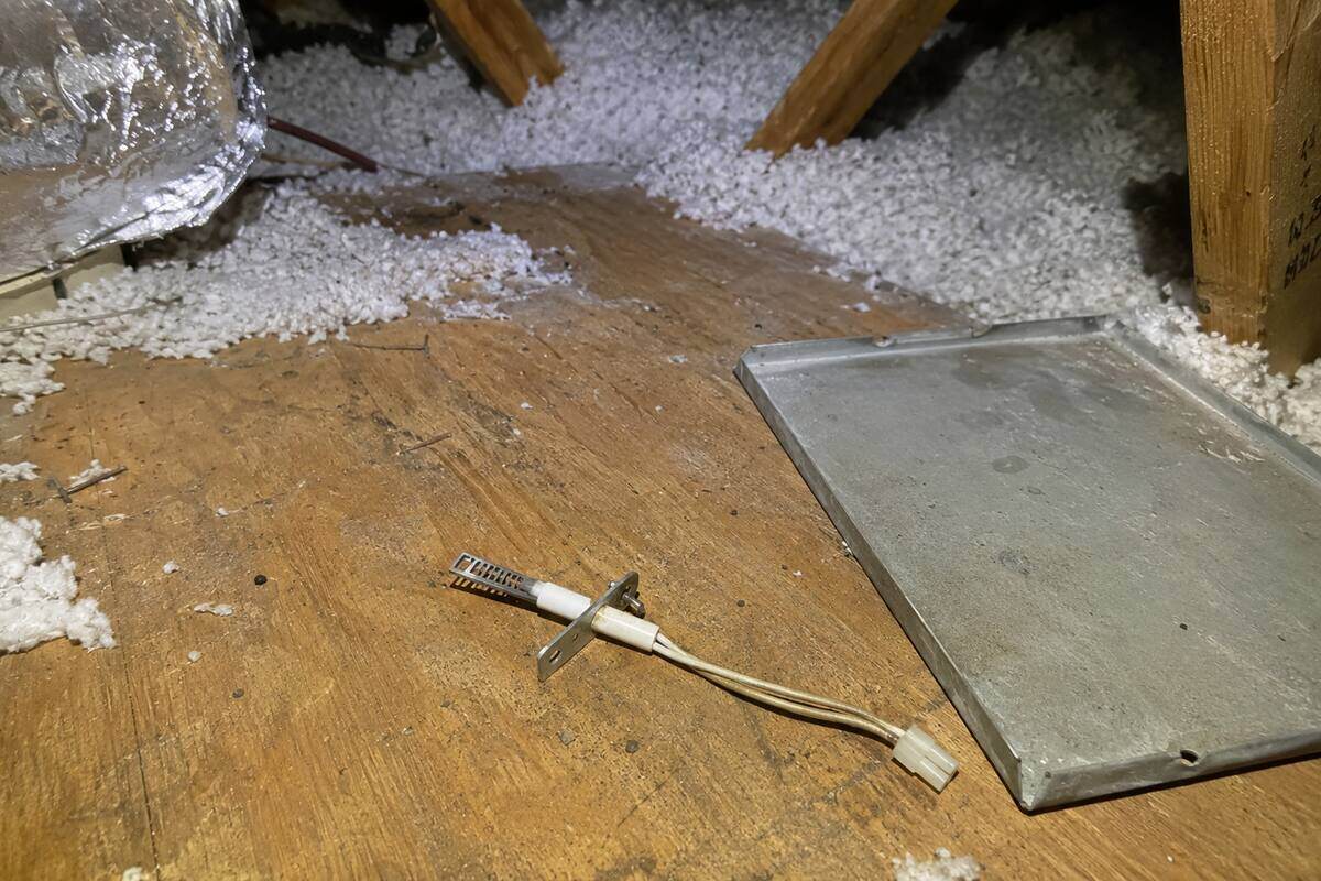 Hot-surface igniter element lying on plywood attic decking beside a removed furnace access panel