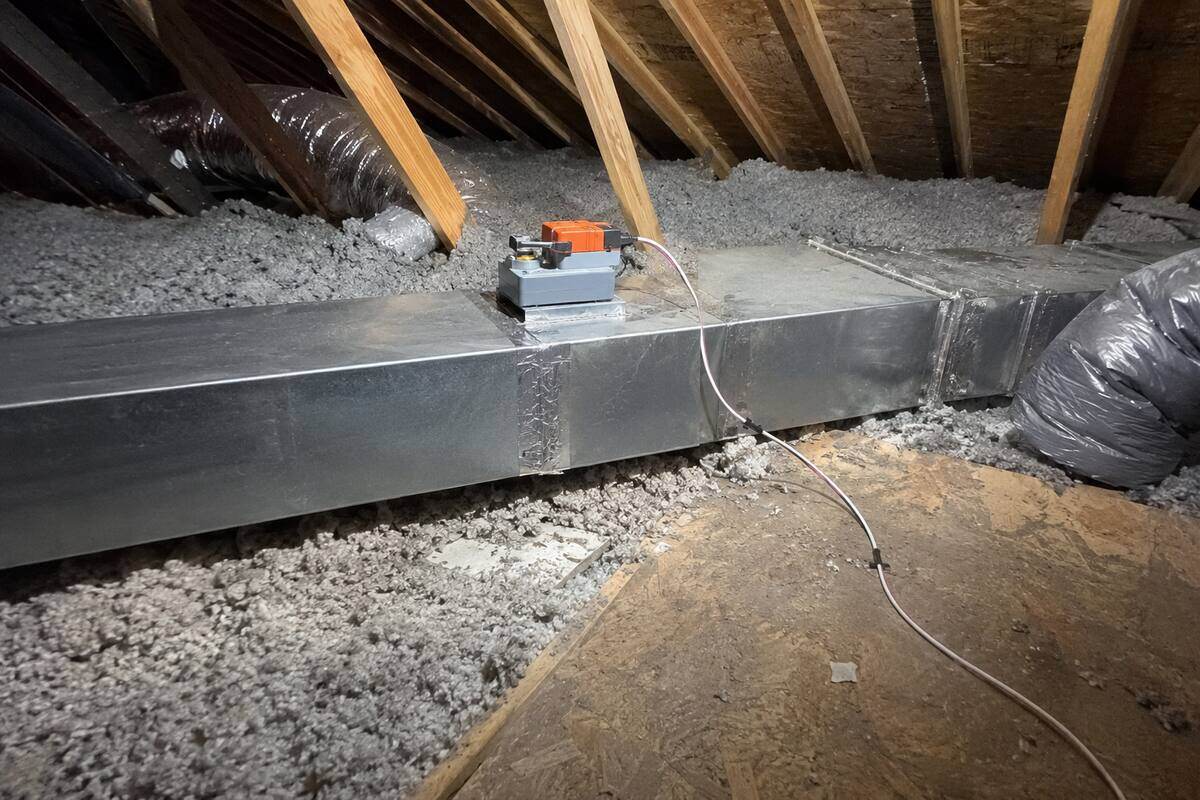 Motorized zone damper fitted into a rectangular duct branch in an attic, control wiring running from its actuator
